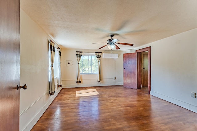 empty room featuring a textured ceiling, hardwood / wood-style flooring, a wall mounted AC, and ceiling fan