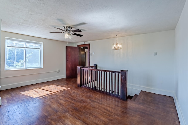 empty room featuring ceiling fan with notable chandelier, dark wood-type flooring, and a textured ceiling