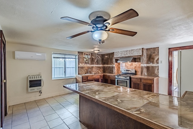 kitchen with a textured ceiling, heating unit, a wall unit AC, white fridge, and stainless steel range with gas cooktop