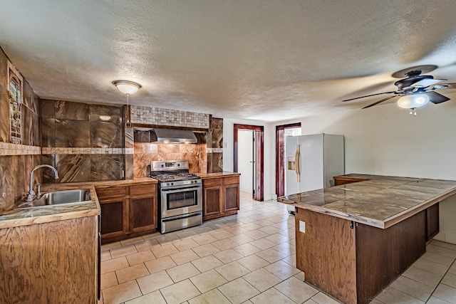 kitchen with a textured ceiling, stainless steel gas range oven, white fridge with ice dispenser, and sink