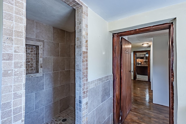 bathroom with a textured ceiling, tiled shower, tile walls, and hardwood / wood-style flooring