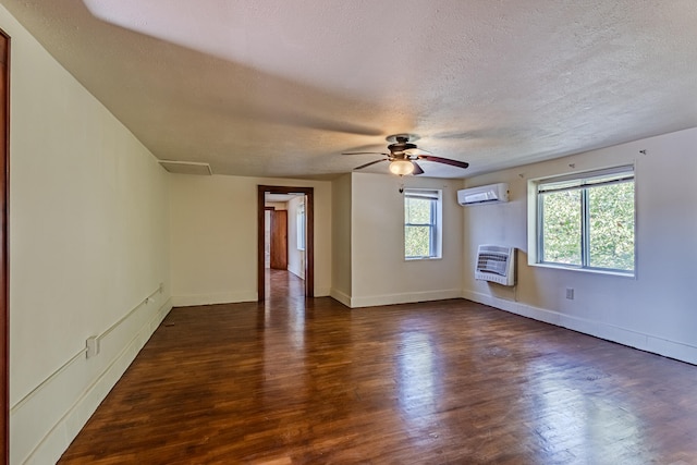 spare room with a textured ceiling, heating unit, a wall unit AC, ceiling fan, and dark wood-type flooring