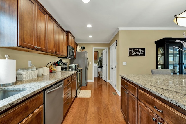 kitchen with light wood-style flooring, crown molding, baseboards, stainless steel appliances, and washer / dryer