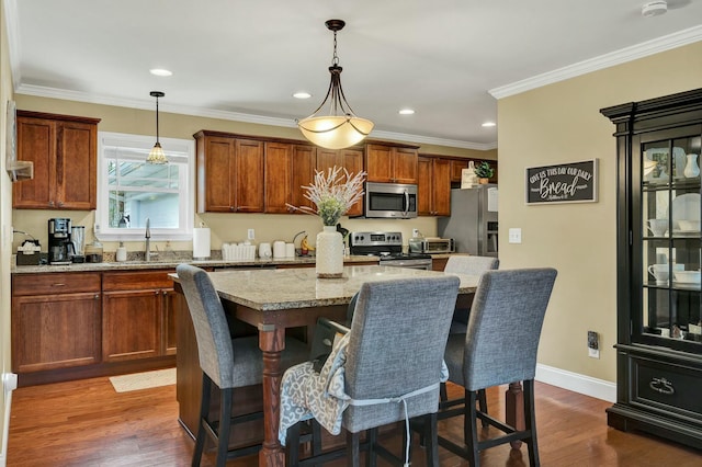 kitchen with a breakfast bar, ornamental molding, stainless steel appliances, dark wood finished floors, and a center island