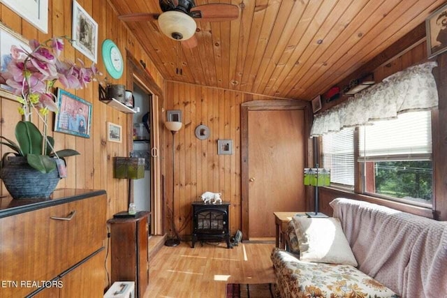 sitting room with wood ceiling, a wood stove, ceiling fan, wooden walls, and light wood-type flooring