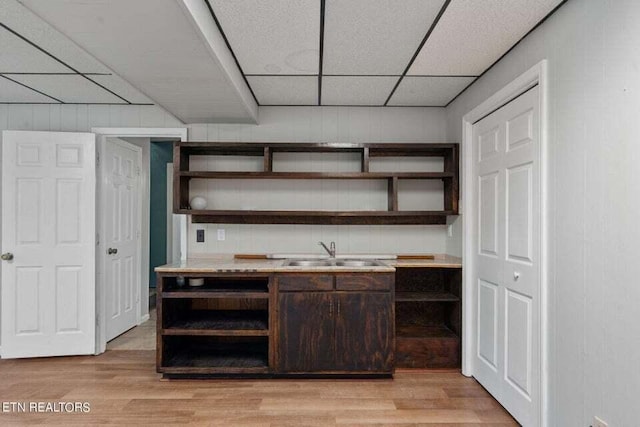 bar with sink, a drop ceiling, dark brown cabinetry, and light hardwood / wood-style flooring