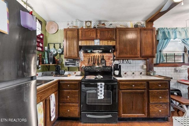 kitchen featuring black / electric stove, decorative backsplash, range hood, and refrigerator