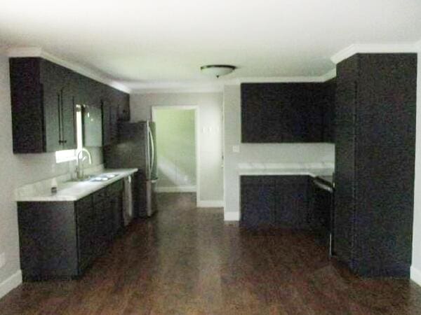 kitchen featuring baseboards, ornamental molding, dark wood-type flooring, light countertops, and a sink