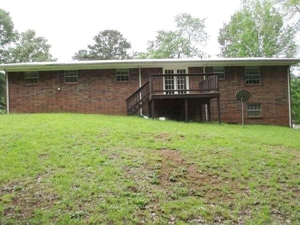 back of property featuring a deck, a lawn, and brick siding
