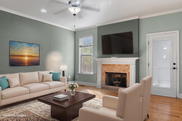 living room featuring a tile fireplace, ornamental molding, ceiling fan, and light hardwood / wood-style floors