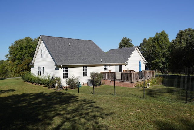 back of house featuring a lawn, a wooden deck, and roof with shingles