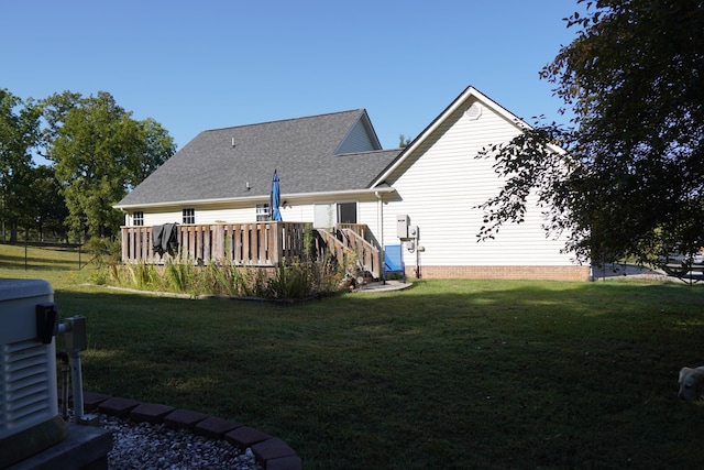 rear view of house featuring a yard, roof with shingles, and a deck