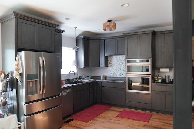 kitchen with light wood-style flooring, a sink, decorative light fixtures, dark countertops, and appliances with stainless steel finishes