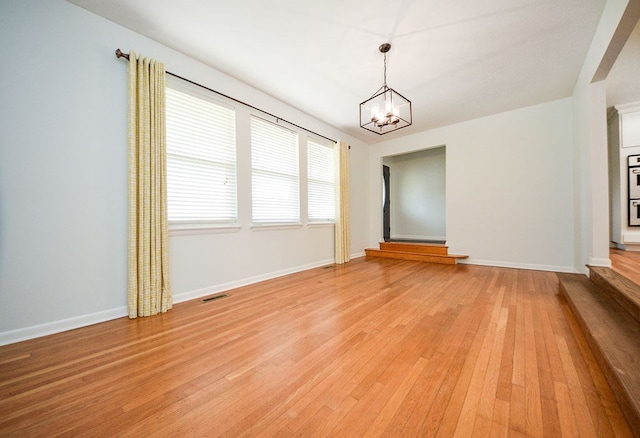 spare room featuring an inviting chandelier and light wood-type flooring