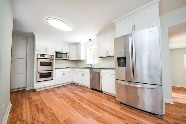 kitchen with backsplash, appliances with stainless steel finishes, decorative light fixtures, light hardwood / wood-style floors, and white cabinetry