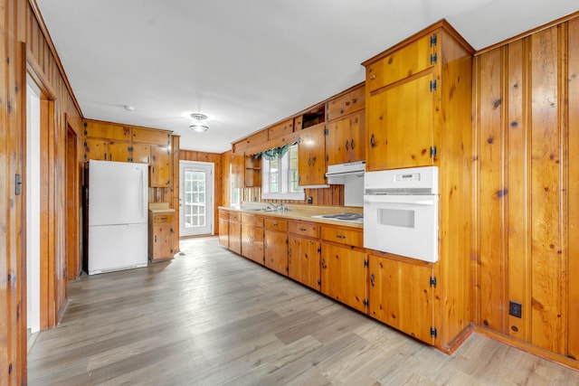 kitchen featuring light wood-type flooring, white appliances, sink, and wood walls