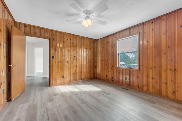 unfurnished room featuring ceiling fan, wood walls, and light wood-type flooring