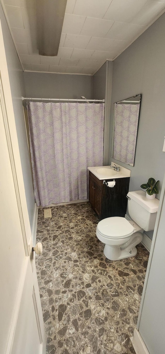 full bathroom featuring curtained shower, stone finish flooring, toilet, and vanity