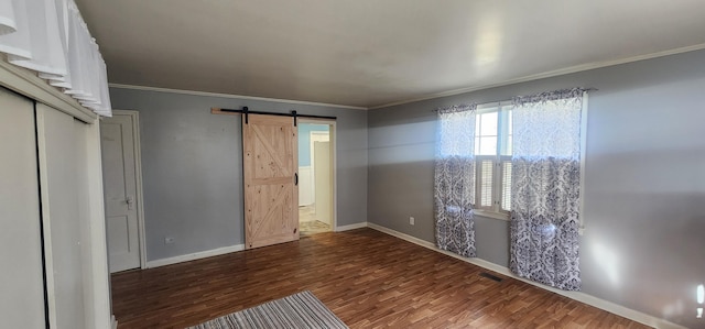 interior space with wood finished floors, baseboards, visible vents, crown molding, and a barn door