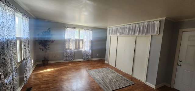 unfurnished bedroom featuring wood finished floors, baseboards, visible vents, ornamental molding, and a closet