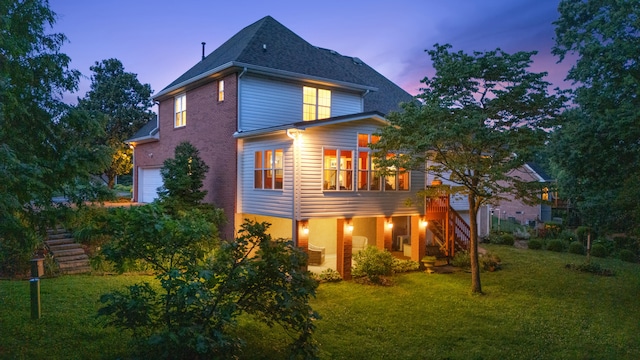 1028 Ivy Manor Ct, Hixson, TN 37343 - back of house at dusk featuring stairs, a garage, a yard, a shingled roof, and brick siding