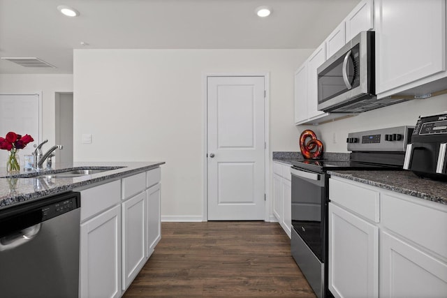 kitchen with dark wood-type flooring, dark stone countertops, stainless steel appliances, white cabinetry, and a sink