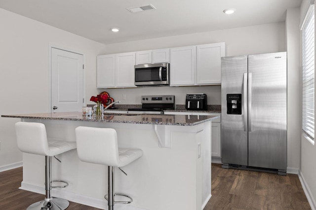 kitchen featuring a breakfast bar area, dark wood-type flooring, white cabinetry, appliances with stainless steel finishes, and dark stone counters