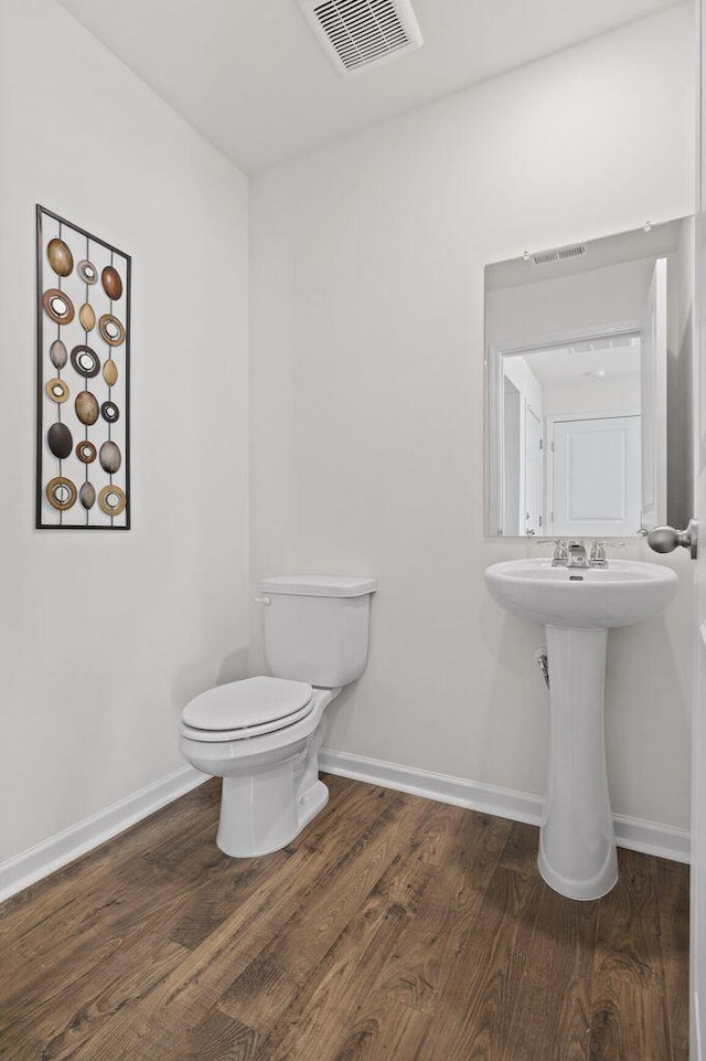 half bathroom featuring toilet, wood finished floors, visible vents, and baseboards