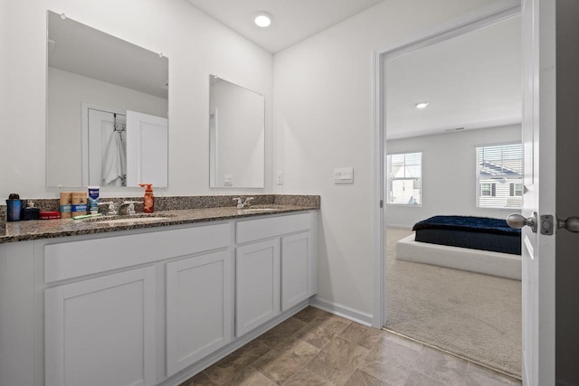 ensuite bathroom with ensuite bathroom, double vanity, a sink, and baseboards