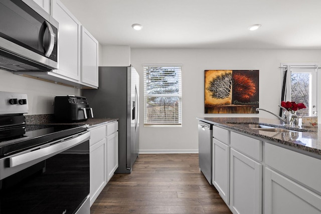 kitchen with dark wood-style floors, stainless steel appliances, white cabinetry, a sink, and dark stone counters