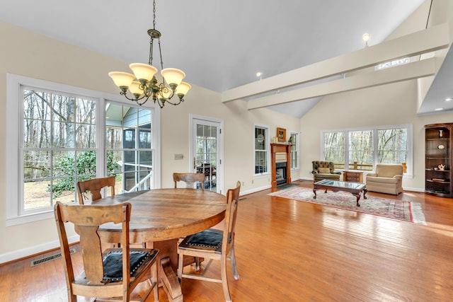 dining space featuring lofted ceiling with beams, plenty of natural light, hardwood / wood-style floors, and a glass covered fireplace