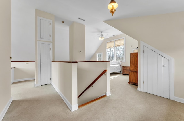 hallway with visible vents, baseboards, light colored carpet, lofted ceiling, and an upstairs landing