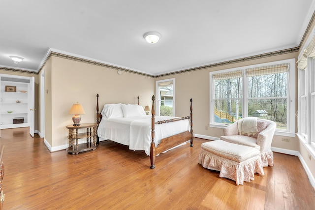 bedroom with light wood finished floors, multiple windows, baseboards, and ornamental molding