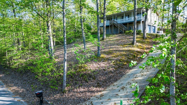 view of yard featuring a garage, a wooded view, a wooden deck, and stairs