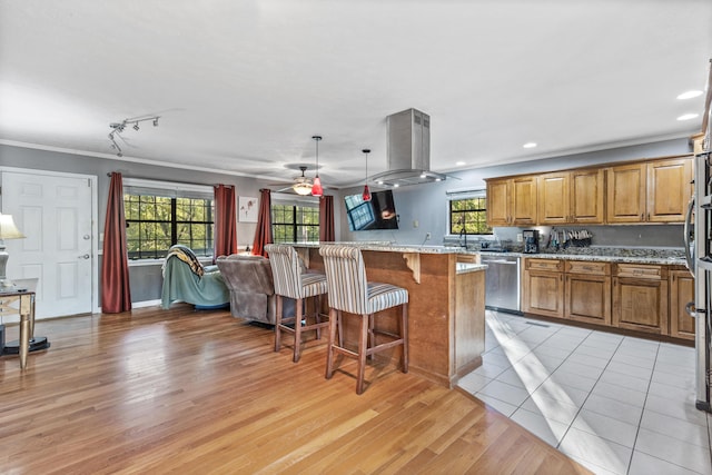 kitchen with brown cabinets, dishwasher, light wood-type flooring, crown molding, and a breakfast bar area