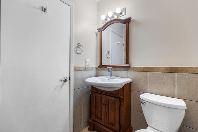 bathroom featuring tile walls, toilet, vanity, and a wainscoted wall