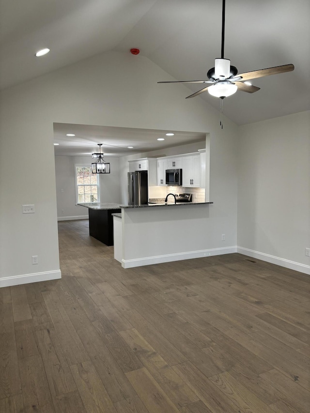 kitchen featuring dark wood-type flooring, vaulted ceiling, white cabinetry, kitchen peninsula, and stainless steel appliances