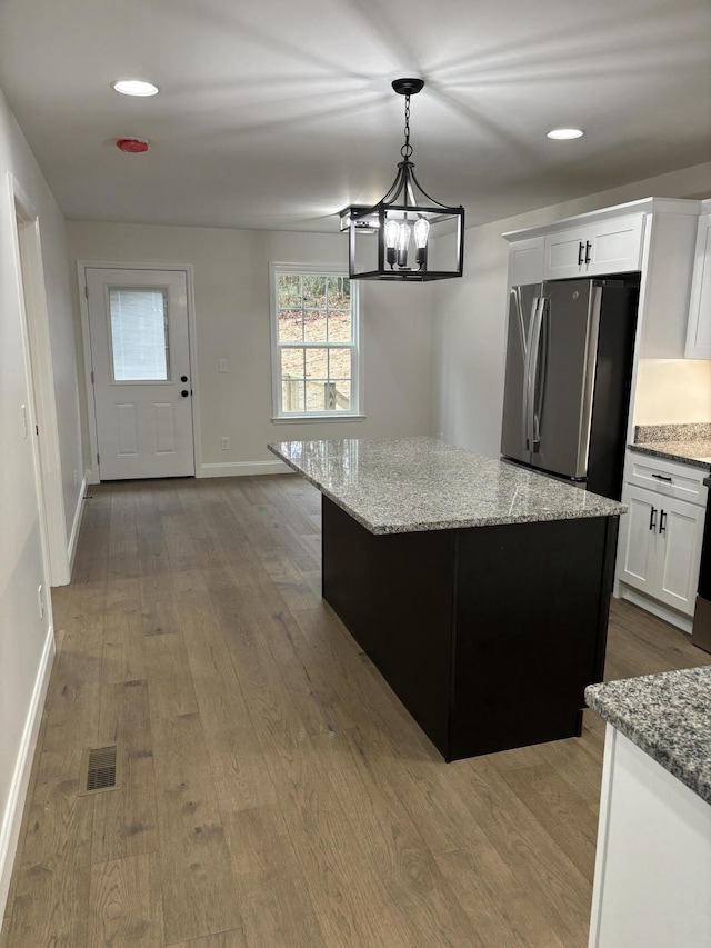 kitchen featuring hardwood / wood-style floors, white cabinets, a kitchen island, light stone counters, and stainless steel refrigerator