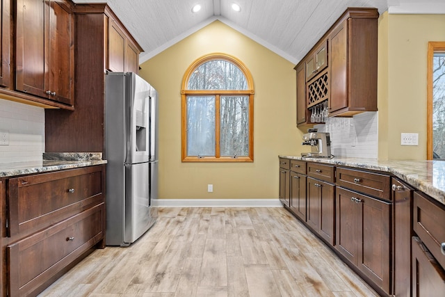 kitchen with decorative backsplash, stainless steel fridge with ice dispenser, light stone counters, and vaulted ceiling