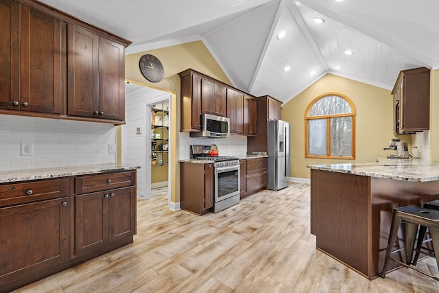 kitchen featuring lofted ceiling, a breakfast bar area, light stone countertops, light wood-type flooring, and stainless steel appliances