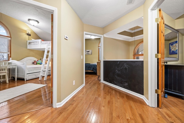 corridor with light wood-type flooring, a textured ceiling, and ornamental molding