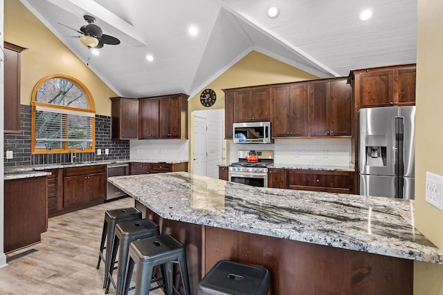 kitchen with stainless steel appliances, light stone counters, ceiling fan, and lofted ceiling