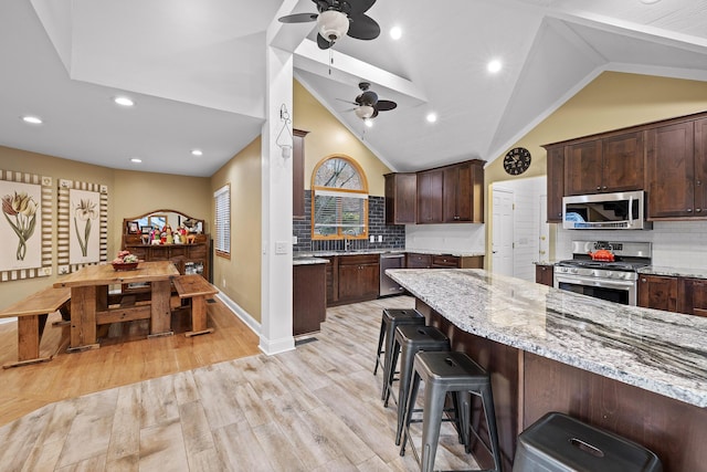 kitchen with light stone countertops, ceiling fan, stainless steel appliances, backsplash, and lofted ceiling