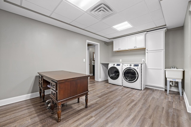 laundry area with washing machine and clothes dryer, cabinets, and light wood-type flooring