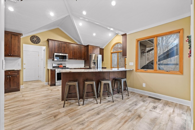 kitchen featuring kitchen peninsula, stainless steel appliances, vaulted ceiling, and tasteful backsplash