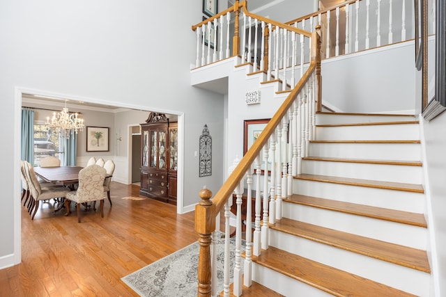 stairway with hardwood / wood-style floors, a towering ceiling, and an inviting chandelier