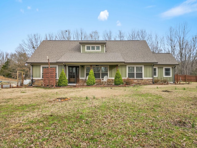 view of front facade with board and batten siding, roof with shingles, fence, and a front lawn