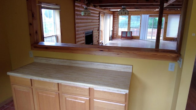 kitchen with light brown cabinetry, plenty of natural light, log walls, and a fireplace