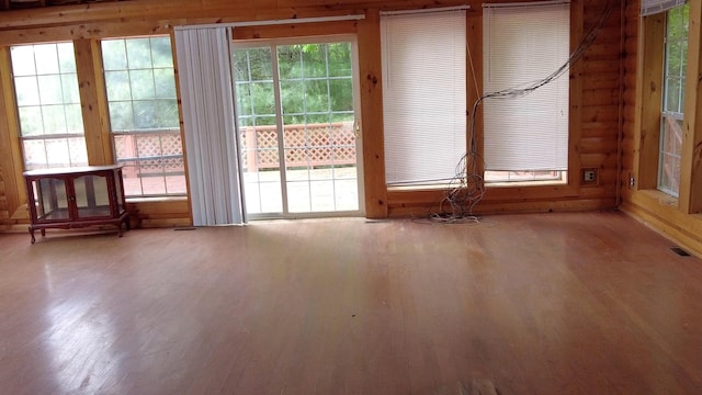 empty room with log walls, hardwood / wood-style floors, and plenty of natural light