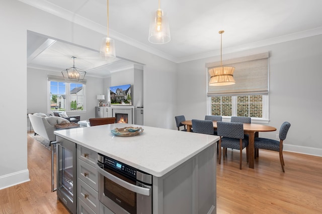 kitchen with gray cabinetry, crown molding, light hardwood / wood-style floors, a kitchen island, and hanging light fixtures